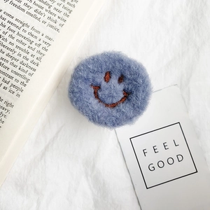 Close-up of blue plush smiley face accessory with fluffy texture on white fabric