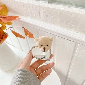 Close-up of heart-shaped phone mirror with rhinestone border and plush bear charm