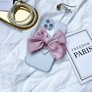 Detail of iPhone case with large pink satin bow and pearl heart charm on white fabric