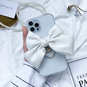 Detail of clear iPhone case featuring a large white satin bow and pearl heart pendant
