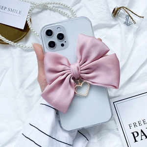 Detail of clear iPhone case featuring a large pink satin bow and pearl heart pendant