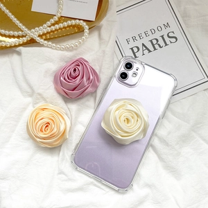 Detailed view of satin rose flower phone grips in white, pink, and orange on silk fabric