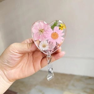 Close-up of heart-shaped resin badge reel with pink daisies and real dried flowers