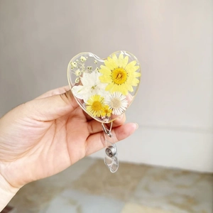 Detail of heart resin badge reel with real yellow and white dried flowers inside