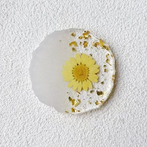 Detail of resin coaster featuring real yellow daisy flower and gold foil gold flakes
