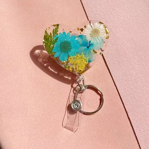 Heart-shaped resin badge reel with blue and yellow dried flowers and gold foil accents