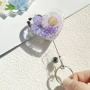 Detail of heart-shaped retractable badge reel with real purple dried flowers in resin