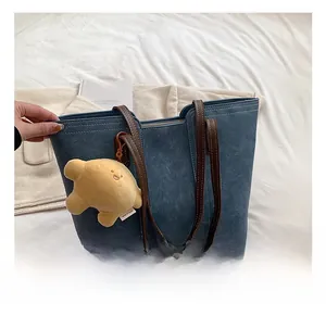 Detail of denim blue tote bag showing brown leather handles and yellow plush bear charm
