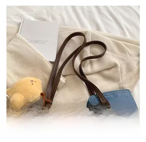 Blue denim tote bag detail featuring brown leather handles and yellow bird charm