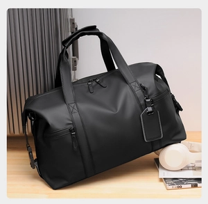 Detail of waterproof black travel bag with sturdy handles and luggage tag on desk