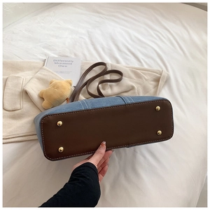 Detail of color-block tote bag bottom with denim fabric and four golden metal feet studs