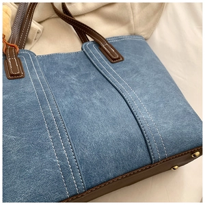 Detail of blue denim tote bag with brown leather base and gold protective feet