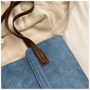 Close-up of blue denim tote bag with brown leather strap and contrast stitching details