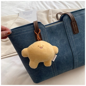 Detail of yellow croissant plush charm with smiling face on a denim tote bag