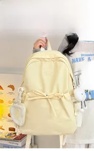 Detail view of cream beige backpack with bow ribbons and cute plush doll charms