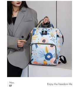 Close-up of a blue floral diaper backpack worn by a model in a stylish grey suit jacket