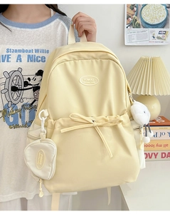 Detail of a light yellow nylon backpack with decorative bow and cute heart coin purse