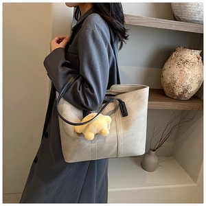 Detail of grey leather tote bag with black straps and yellow puppy plush charm