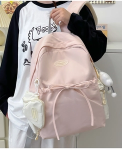 Detail of pink student backpack featuring a silk bow and heart-shaped coin purse