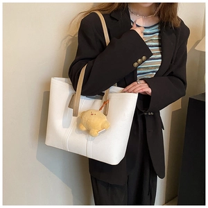 White leather tote bag with brown straps and cute yellow plush charm on model