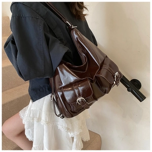 Detail of dark brown patent leather hobo bag with front pockets and metallic buckles