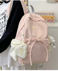 Detail of pink and white school backpack with ribbon bow and heart-shaped pendant bag