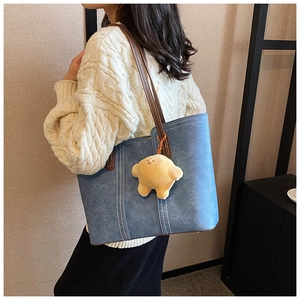 Blue denim tote bag with brown leather handles and a yellow chick plush keychain