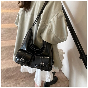 Detail of glossy black tote bag featuring double front flap pockets and silver buckles