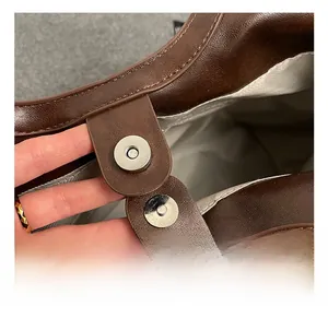Detailed macro view of the silver magnetic buckle on a brown lychee textured leather tote bag