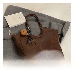 Brown faux leather tote bag with bear charm on grey wool coat and books background