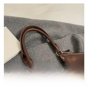 Detail of dark brown leather tote with padded handle, silver hardware and plush bear charm