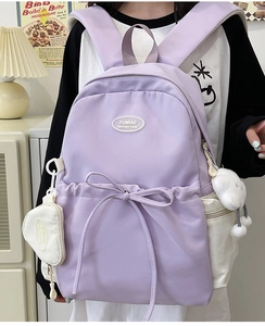 Close-up of lilac nylon backpack featuring a large bow and white heart-shaped mini pouch