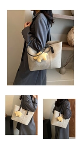 Detail of minimalist beige tote bag with black straps and yellow bear plush keychain