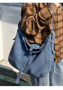 Detail of adjustable metal eyelet straps on a large blue denim hobo shoulder bag