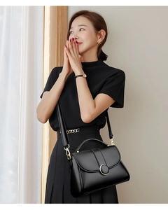 Detail of a black leather handbag with a gold ring buckle styled on a pleated outfit
