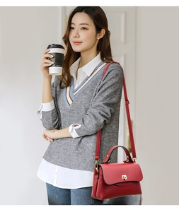 Detail of red pebbled leather handbag with gold clasp, held by woman in city outfit