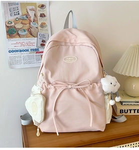 Detail of pink canvas backpack featuring a bow decoration and cute plush cloud pendant
