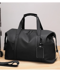 Detail of black waterproof travel bag with reinforced handles and side pockets on a table