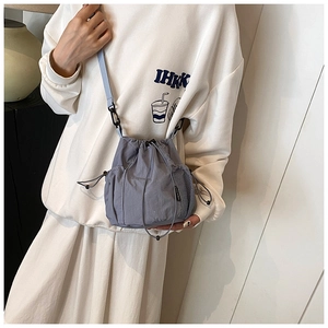 Gray nylon drawstring bucket bag shown on shoulder, featuring side mesh pocket and slim strap