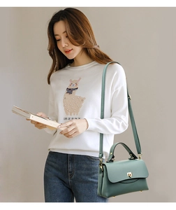 Close-up of dark green lychee grain handbag with gold clasp worn with a casual outfit