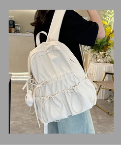 Close-up of cream school backpack with drawstring pockets and cute plush bear charm