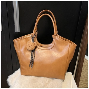 Close-up of brown matte PU leather tote bag with plush bear charm and woven cord detail