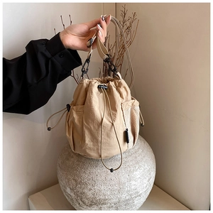 Detail of beige nylon drawstring bucket bag showing side mesh pocket and adjustable strap