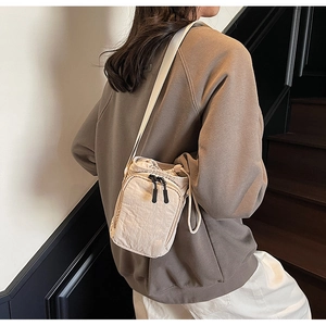 Détail de la sacoche beige en nylon avec texture micro-ridée et tirettes de zip en cordon