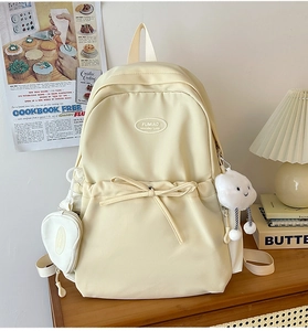 Detail of cream backpack with bow decoration and cute heart-shaped charm on wooden table