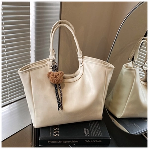 Detail of off-white faux leather tote bag with a brown plush bear charm and dual handles