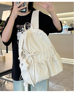 Detail of cream backpack featuring a drawstring pocket, large bow, and cloud charm