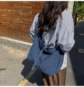Detail view of large denim crossbody tote bag with adjustable grommet strap and casual style