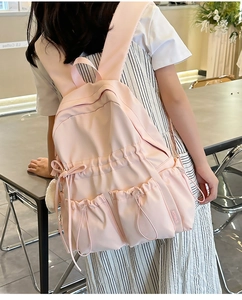 Pink nylon backpack detail showing side drawstring pocket and plush ball ornament