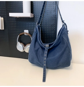 Detail of deep blue denim hobo bag featuring cargo strap and metal eyelet accents